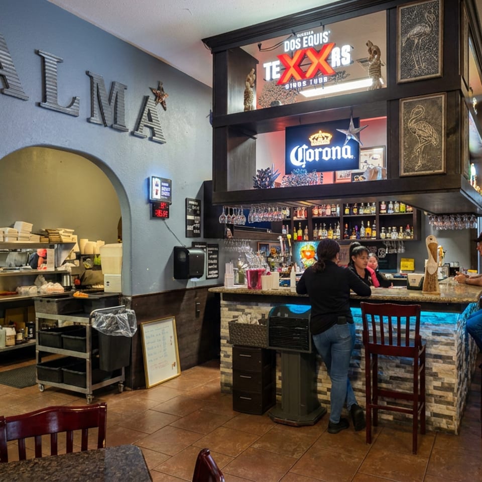 Interior of Dos Equis Tex-Mex restaurant with a stocked bar, seated diners, lunch specials poster, and colorful beer signs.