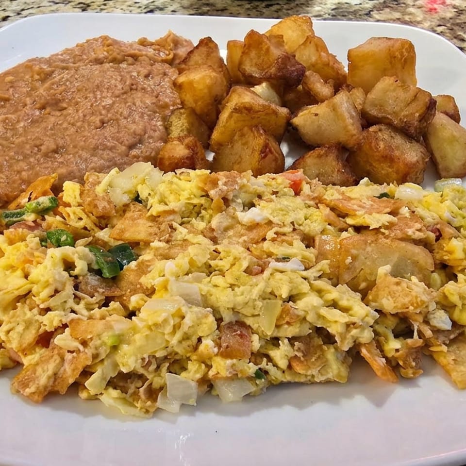 Plate of scrambled eggs with vegetables, refried beans, and golden roasted potatoes on a white dish.