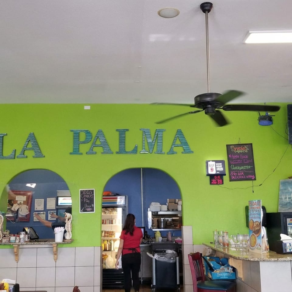 Bright green La Palma restaurant interior with bar, drink taps, ceiling fans, television, and a staff member behind the counter.
