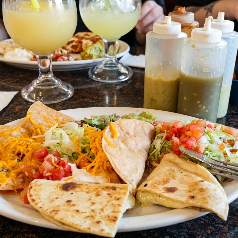 Mexican meal with tacos, quesadillas, nachos, rice, salsa, and guacamole alongside refreshing drinks on a restaurant table.
