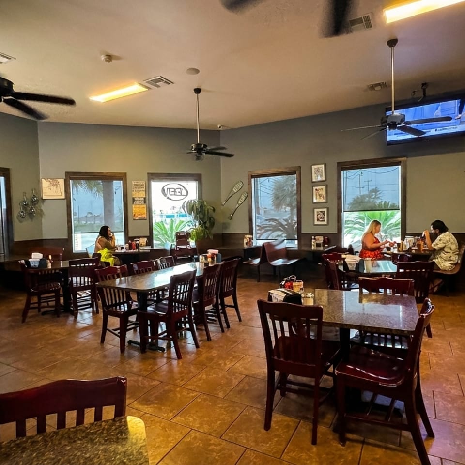 Spacious seafood restaurant dining room with wooden tables, ceiling fans, nautical wall decor, and several diners.