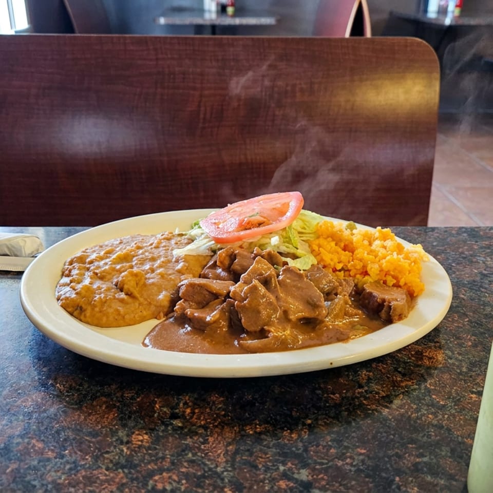 Plate of Mexican-style food with saucy meat, refried beans, yellow rice, lettuce, and tomato in a casual restaurant.