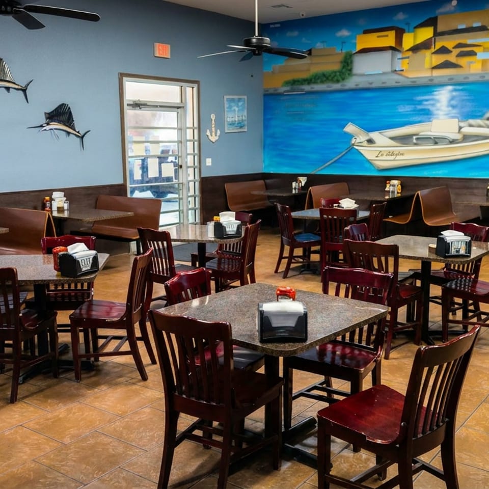 Spacious seafood restaurant dining room with wooden tables, dark red chairs, fish decorations, and a colorful mural of a boat and seaside village.
